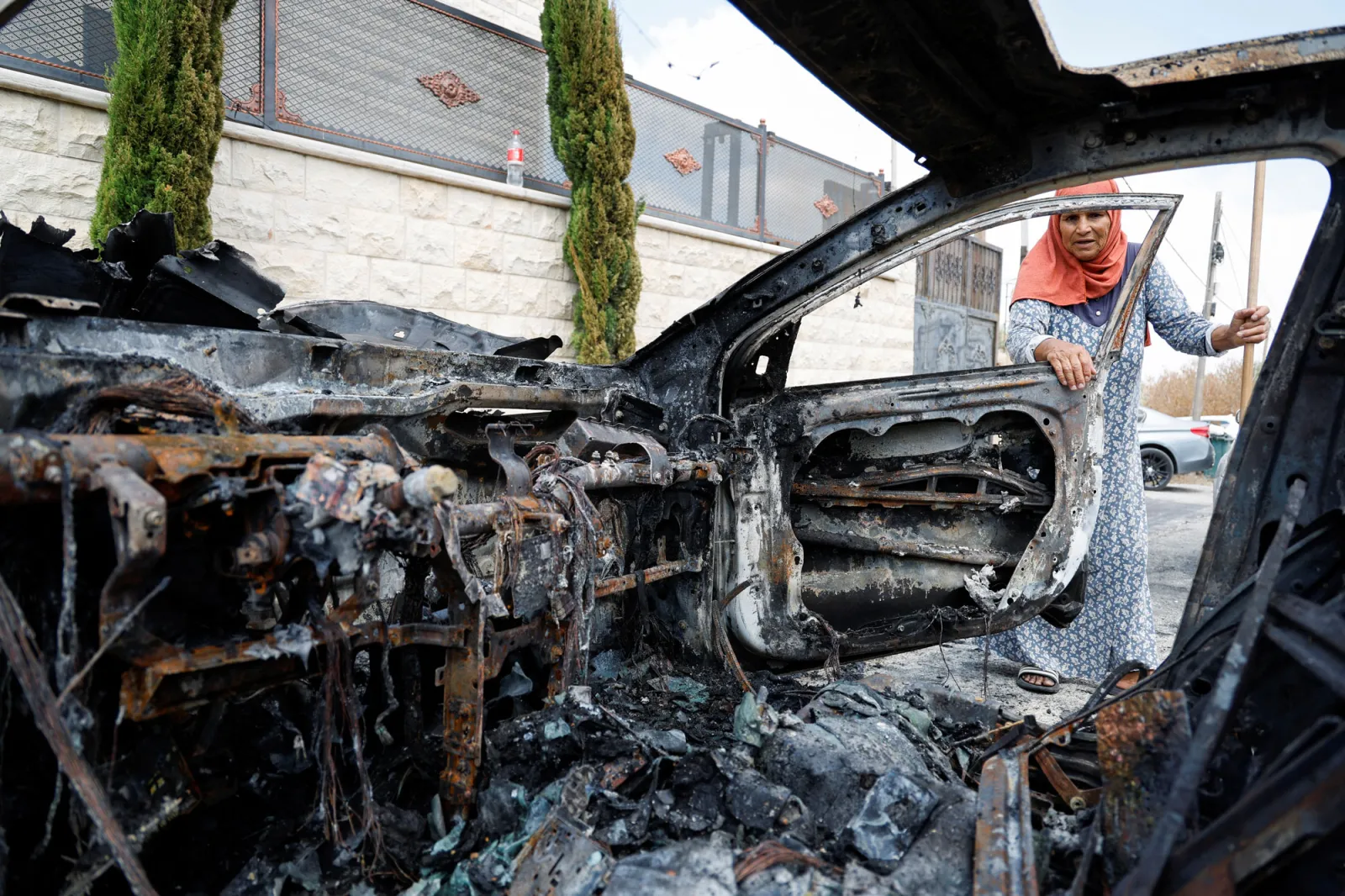 A Palestinian woman inspecting a vehicle destroyed by Israeli settlers, near Qalqilya in the West Bank, August 2024